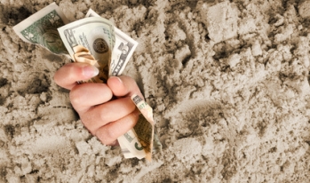 Hand sticking out of sand grasping money Hand sticking out of sand grasping money