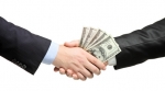Two people shaking hands while holding money Two people shaking hands while holding money
